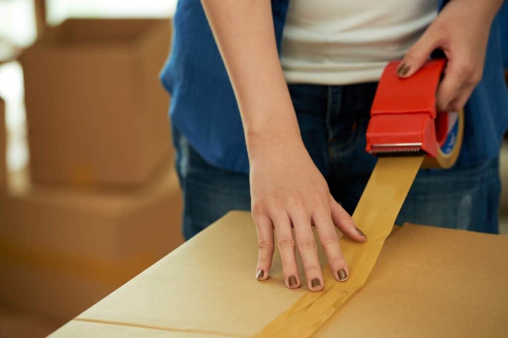 Cropped image of a professional packer sealing cardboard with tape