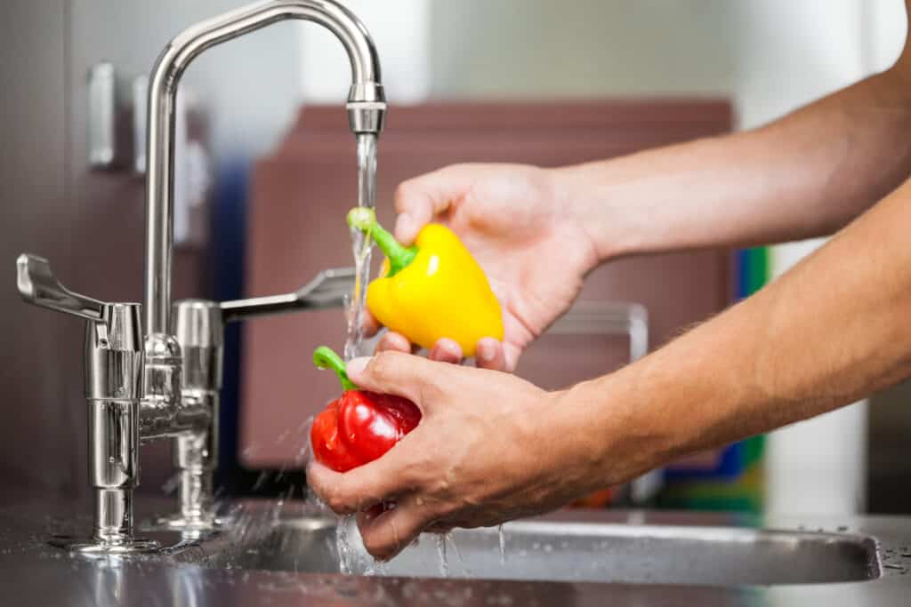 Cropped image of a person washing pepper under tap water